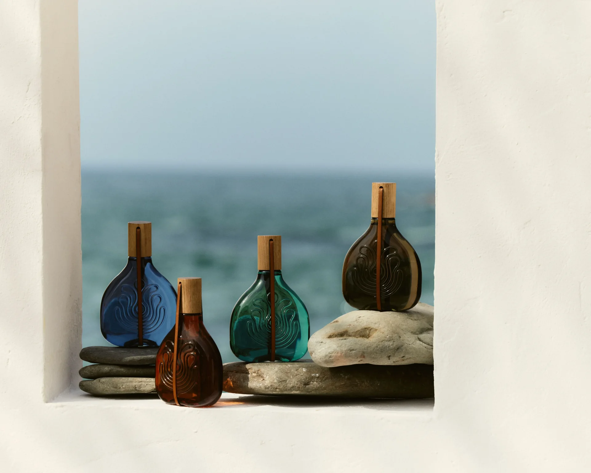 Quatre flacons colorés des Colonias Absolutas Puig face à la mer